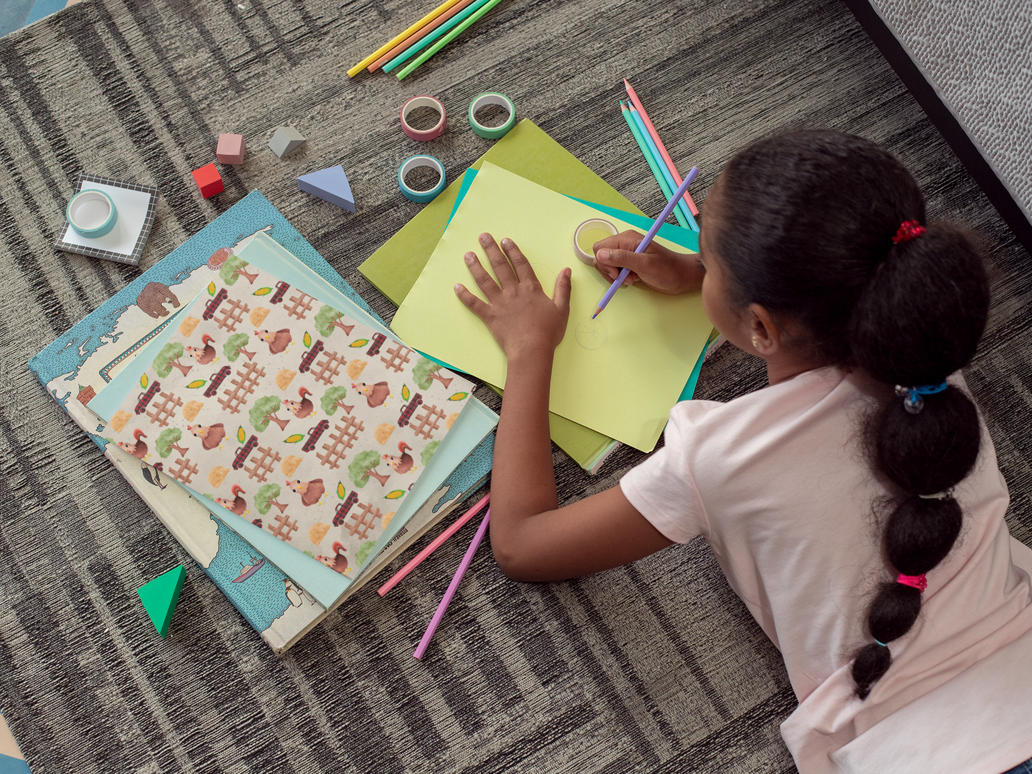 Child drawing on a piece of paper with colorful pencils on a carpeted floor.