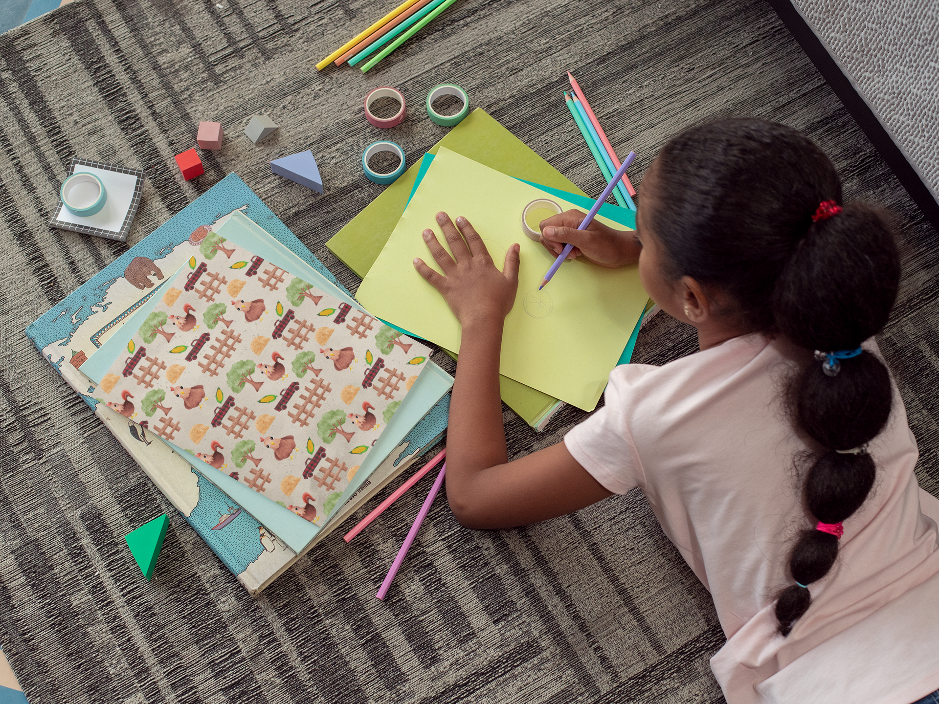 Child drawing on a piece of paper with colorful pencils on a carpeted floor.